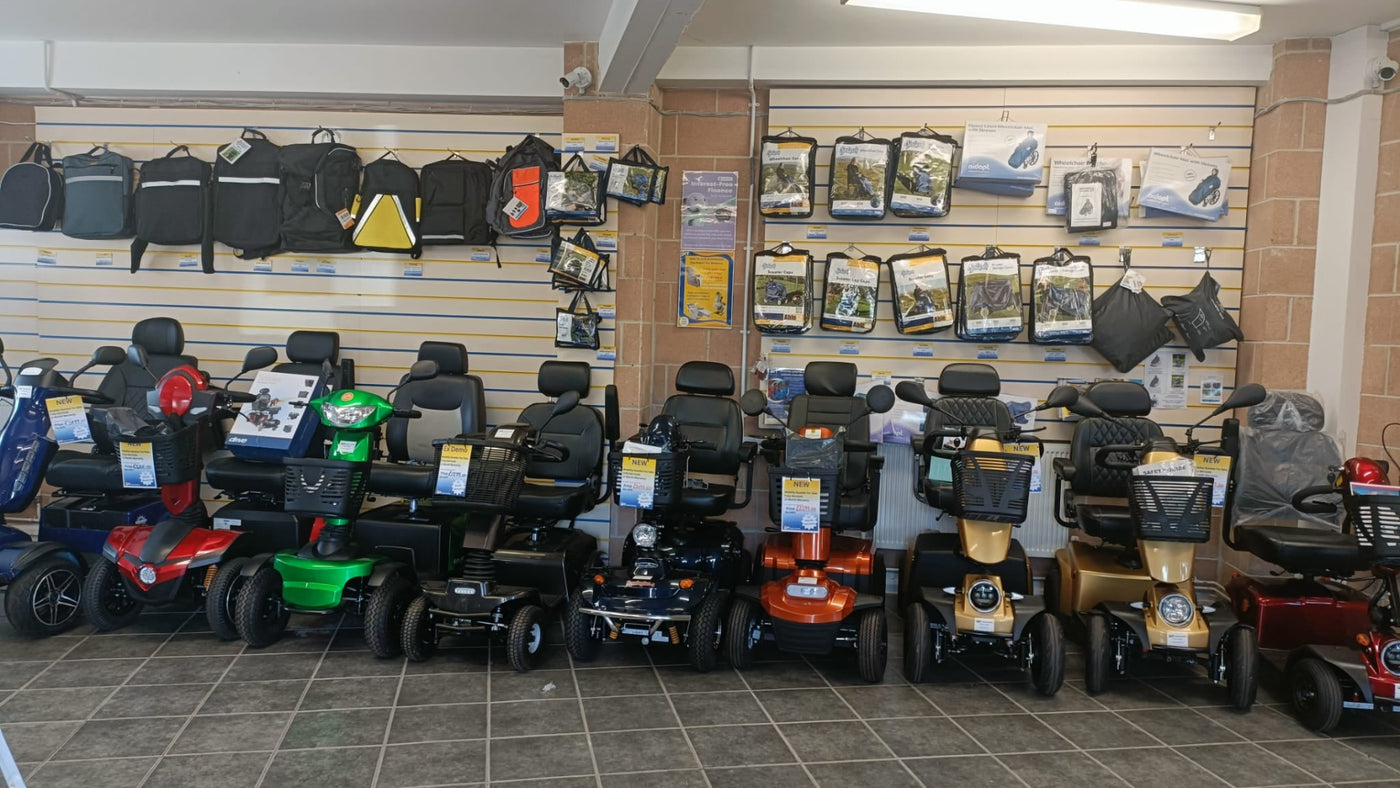 Row of mobility scooters in a showroom with various items on shelves in the background.